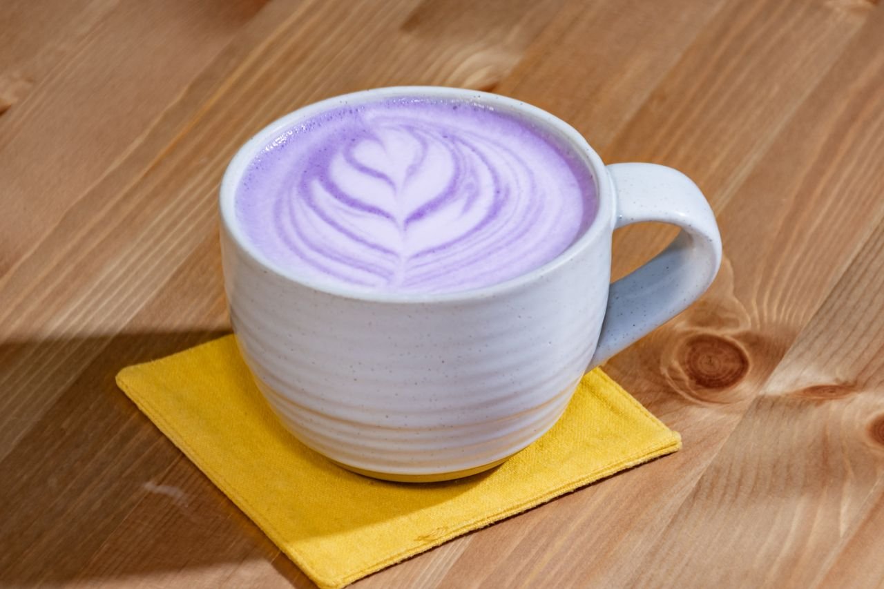 A cup of purple latte with art design in white ceramic mug on wooden table.