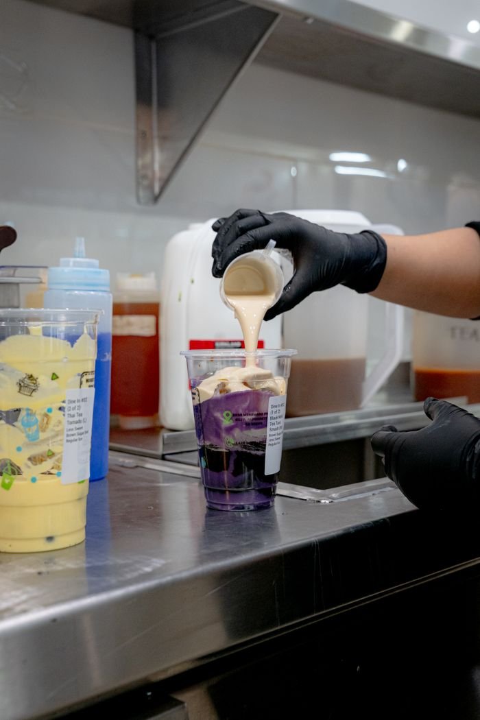 Barista adding cream to vibrant purple bubble tea, creating a flavorful blend.