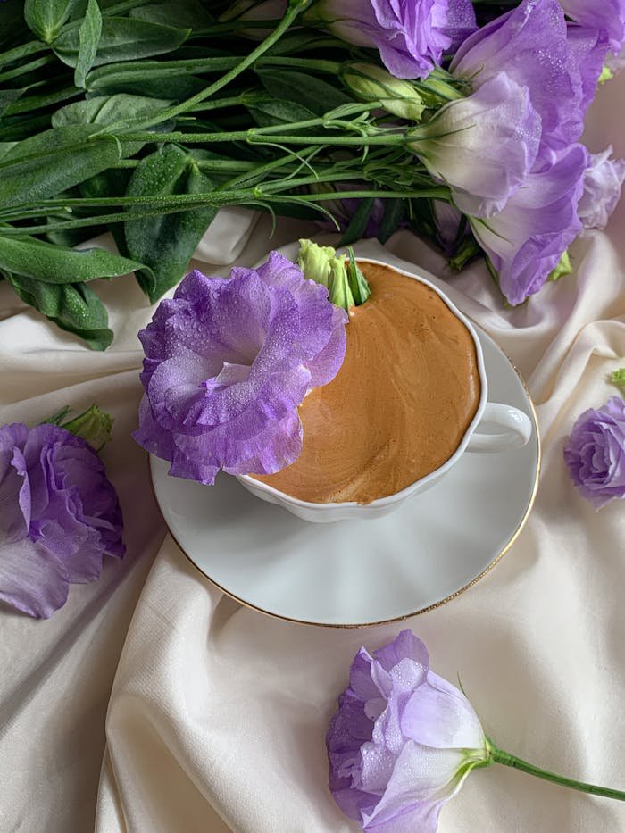 about-002 A cup of coffee elegantly placed amidst purple flowers on a white cloth, creating a serene and calming atmosphere.