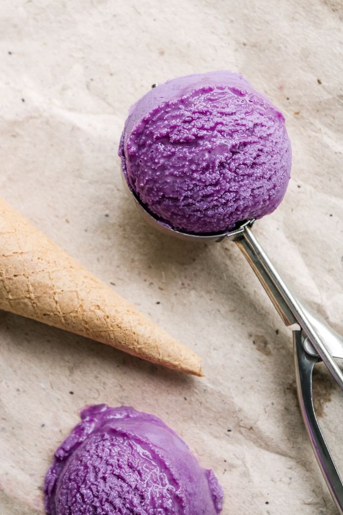 Delicious purple ice cream with cone and metal ice cream scoop on a textured surface.